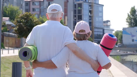 elderly couple walking with yoga mats outdoors