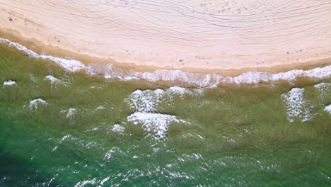 Slow-motion-overhead-drone-clip-over-a-beatiful-beach-with-crystal-waters-and-waves-crushing-on-the-ground-in-Keramoti,-Kavala,Northern-Greece