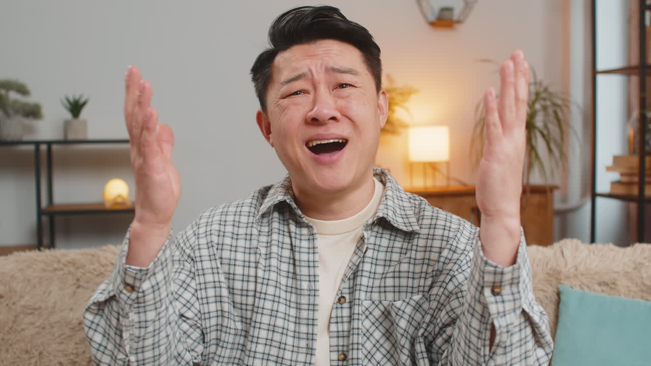 화가 난 중국인 남자가 집에서 소파에서 tv를 보는 결과에 실망한 얼굴을 하고 있습니다.