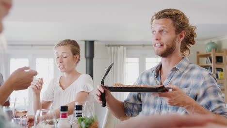 Group-Of-Young-Friends-Sitting-Around-Table-At-Home-Enjoying-Meal-Together