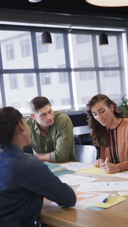 vertical video of diverse male and female colleagues in discussion using notes in casual office