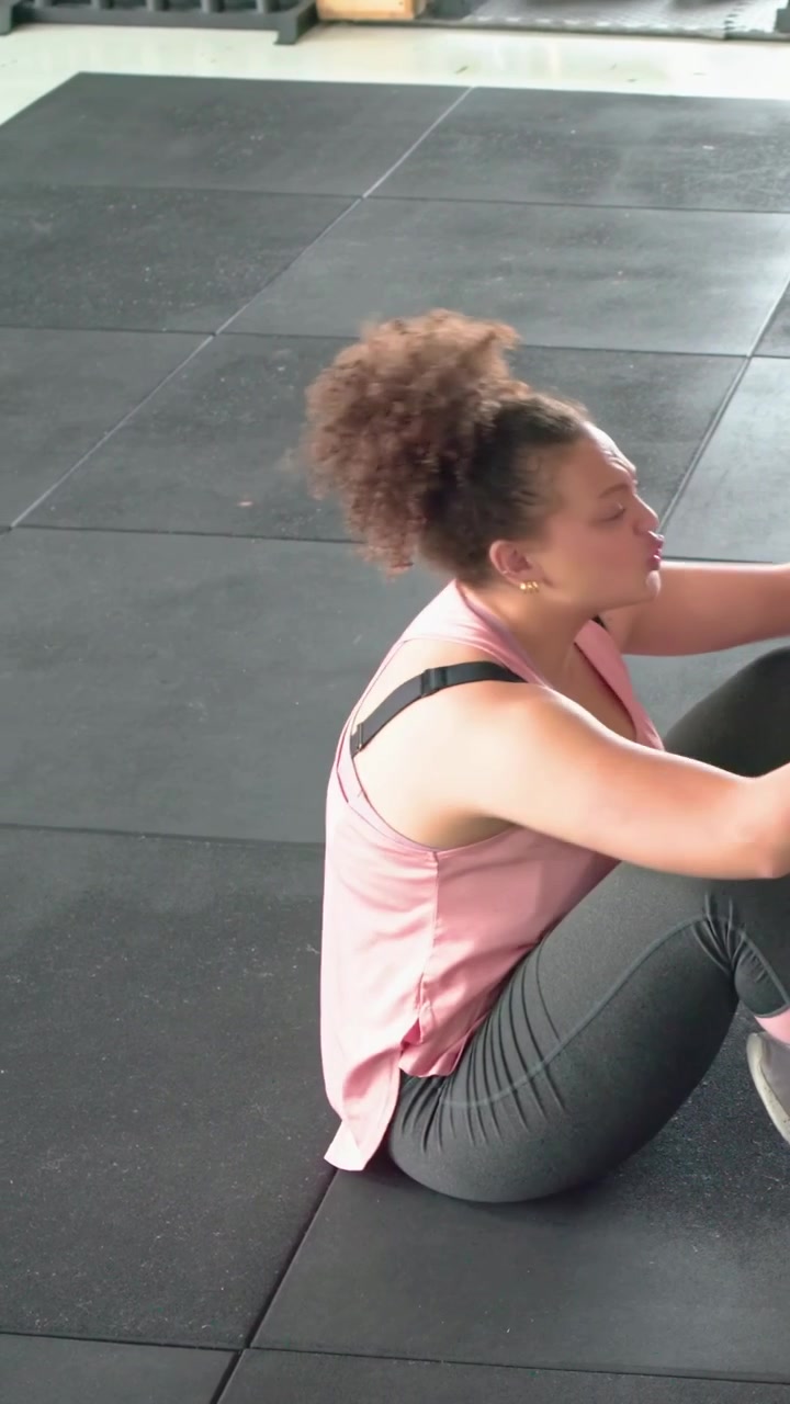 Video verticale: Donna che inizia a fare addominali su un tappetino di gomma da palestra per il core, con canotta rosa e leggings grigi.