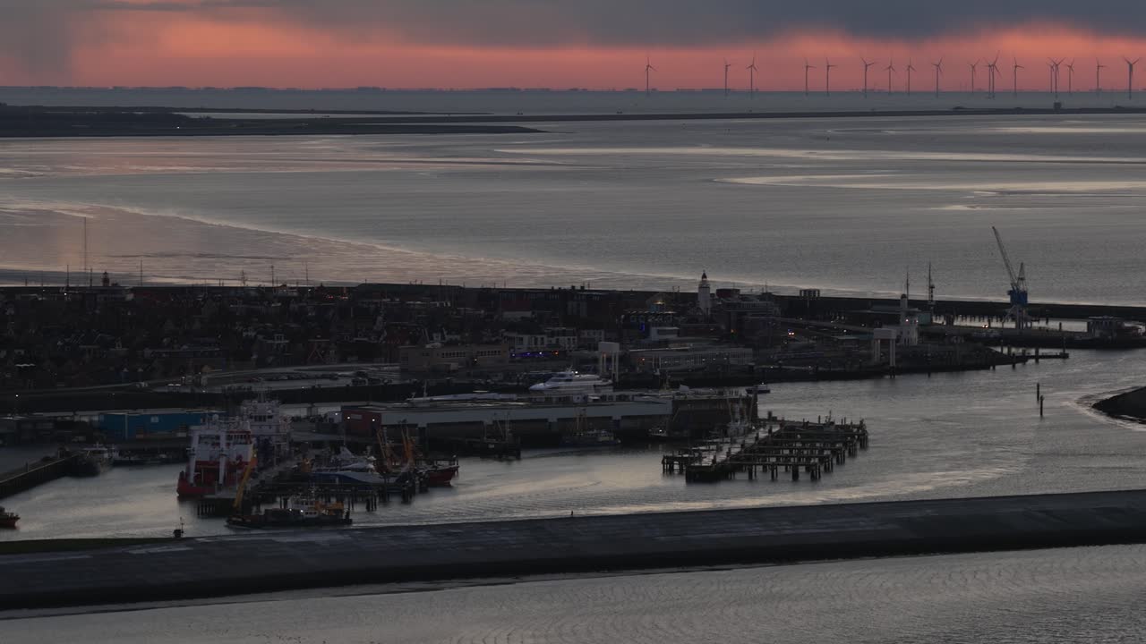 Aerial drone video of the industrial sea port of Harlingen, Friesland, at dusk on the Wadden Sea, showcasing a mix of seagoing vessels, ferries, Brown Fleet historic ships, and official service boats