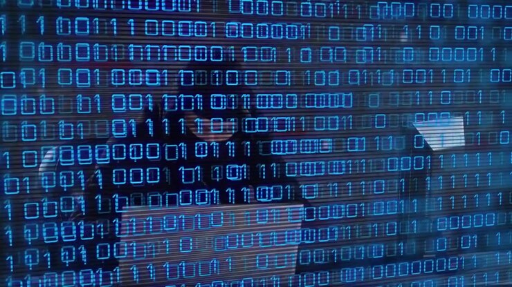 Hacker in Hoodie Typing on Laptop with Digital Binary Code Overlay