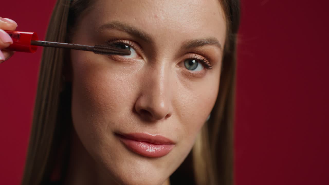 mujer aplicando máscara y sonriendo frente a un fondo rojo