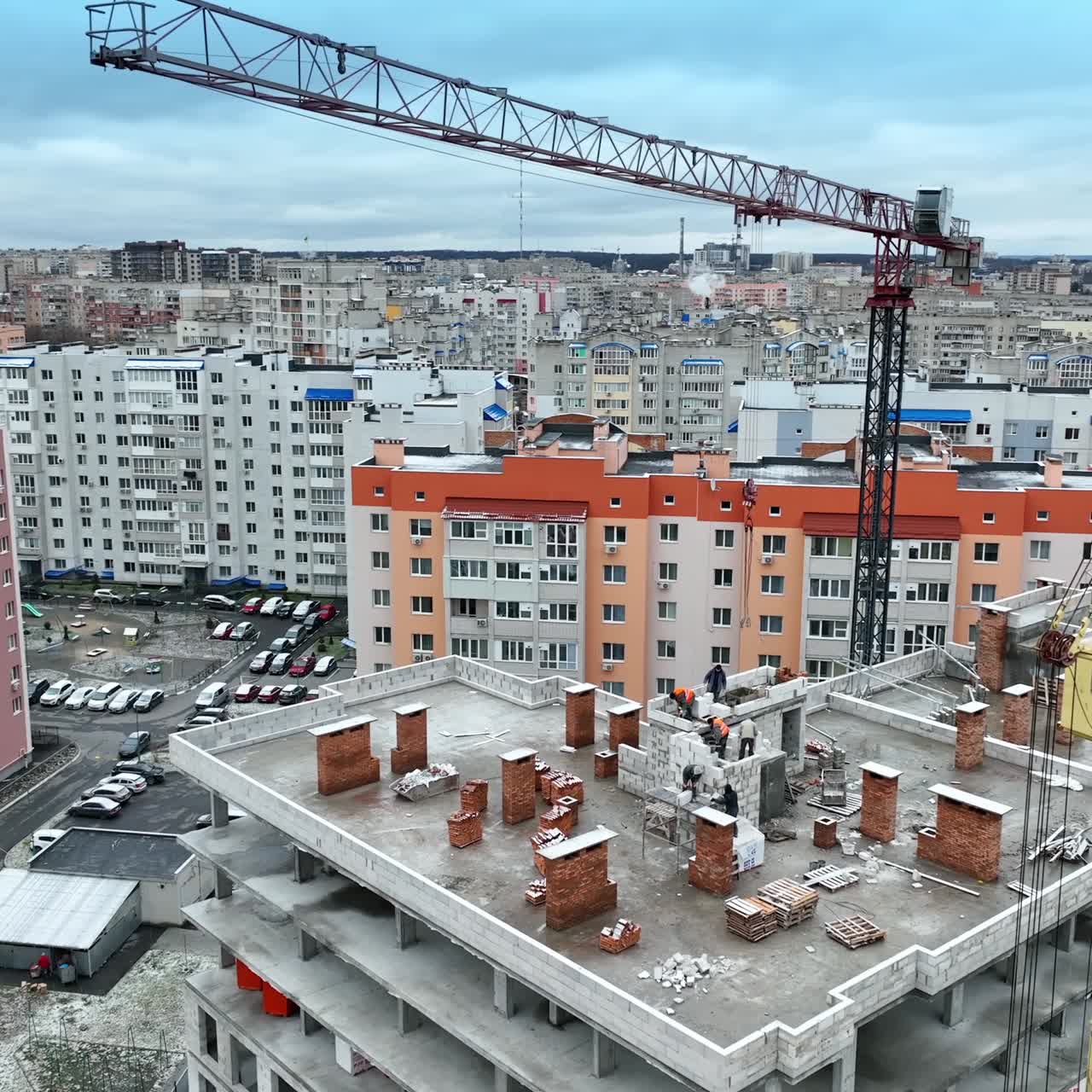 Builders working on the roof of the multi-storied house. High block of flats with construction crane beside. Circle movement footage