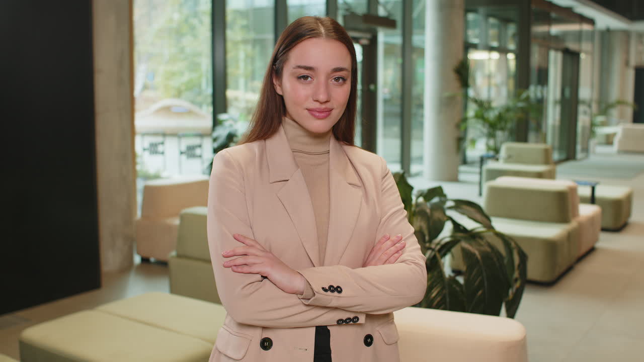 Portrait of happy young businesswoman with arms crossed looking at camera in office hotel lobby