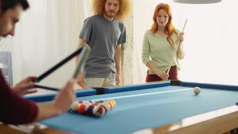 Group of diverse friends playing billiards in apartment