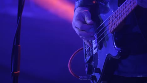 a man in a mask plays an electric bass guitar at a rock concert in a club. nightlife in a big city. red and blue lighting