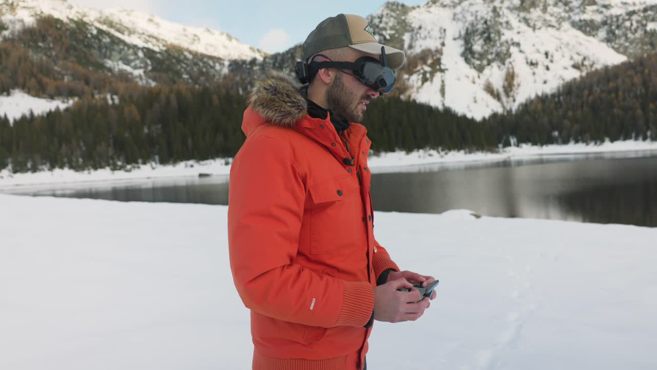 Drone pilot with FPV viewer controlling DJI Avata quadcopter with wireless remote control surrounded by beautiful mountains and snowy landscape