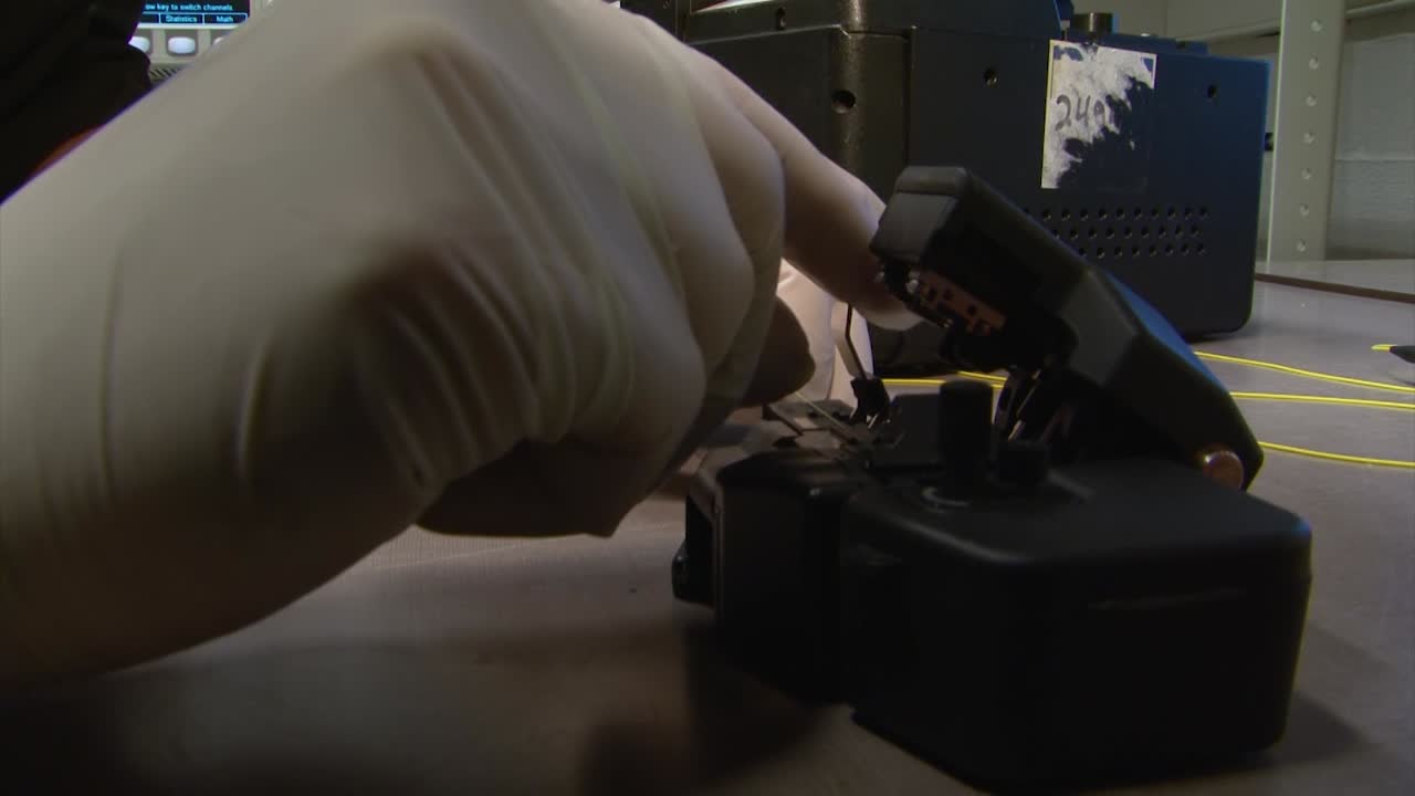 manos poniendo cable de fibra óptica en un cortador de alta precisión en laboratorio fotónico