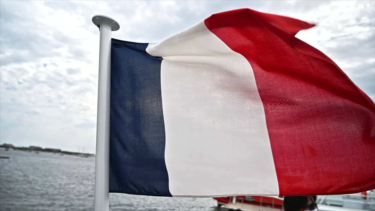 The French flag fluttering in the wind in sea port of Cannes, France. Slow motion