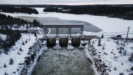 drone out long snow covered road with aerial slow drone orbit rushing water notigi hydroelectric dam in the arctic