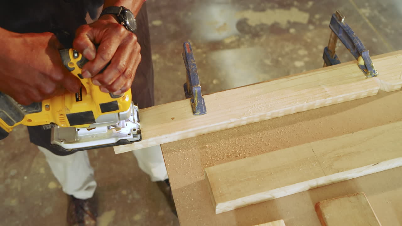 Mature African American carpenter securing plank with clamps guiding router at shop smoothing edge