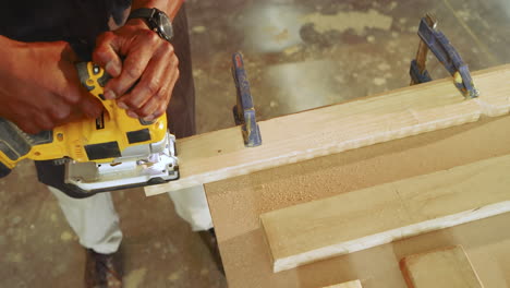 mature african american carpenter securing plank with clamps guiding router at shop smoothing edge