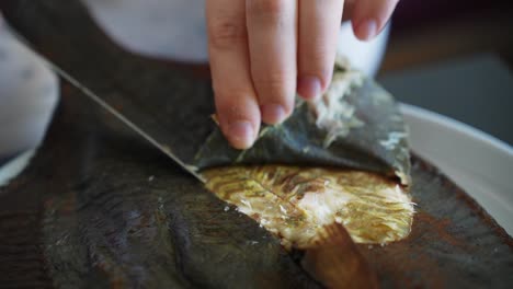 hands of person slowly peeling smoked fish skin off, close up view