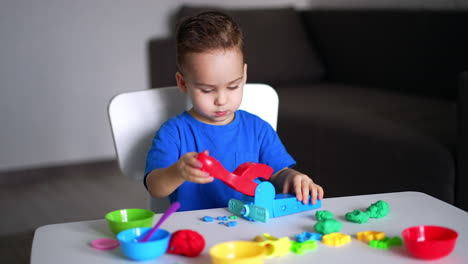 adorable caucasian baby sits at desk at home. lovely kid uses a device to make figures from plasticine.
