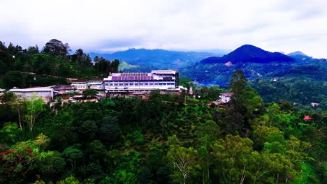 a sri lankan hillside features a prominent solar-paneled building among green trees, rural houses, and expansive mountain views, blending modern architecture with natural landscapes.