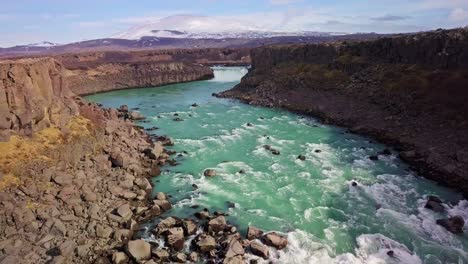 Flyover-river-canyon-with-rushing-rapids-and-waterfall-with-mountain-in-background