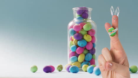 animation of fingers with easter bunny and easter egg over jar of easter eggs on blue background