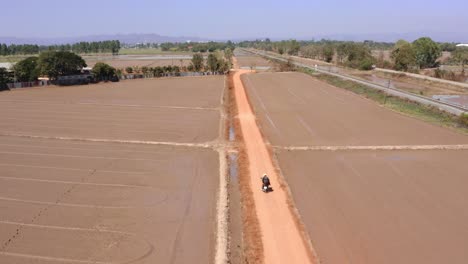 Tracking-Shot-Of-Rider-Driving-Motorcycle-On-Dirt-Rural-Road,-Thailand