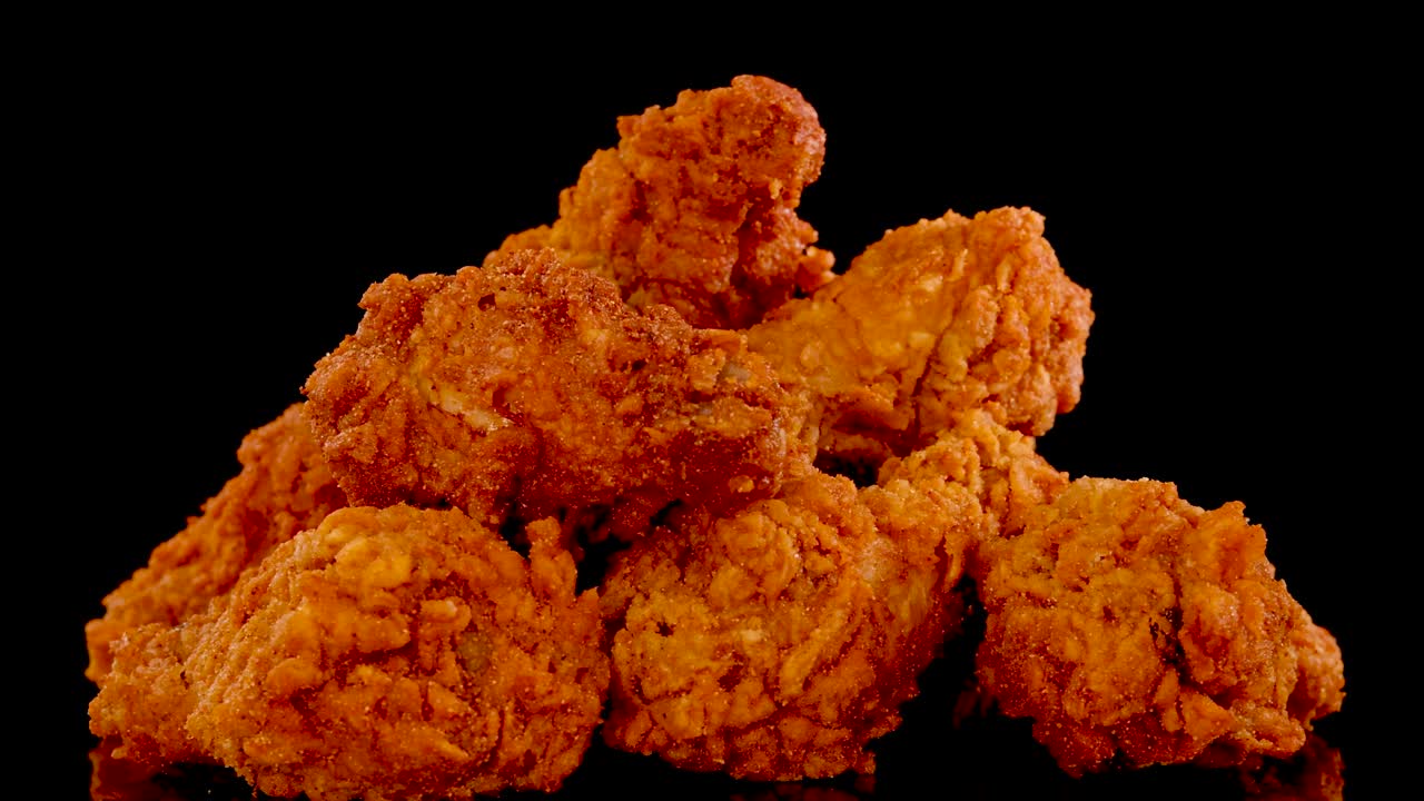 Crispy, golden-brown fried chicken pieces rotate and zoom in slow motion against a black background, highlighting texture and seasoning under dramatic studio lighting