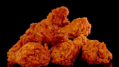 crispy, golden-brown fried chicken pieces rotate and zoom in slow motion against a black background, highlighting texture and seasoning under dramatic studio lighting