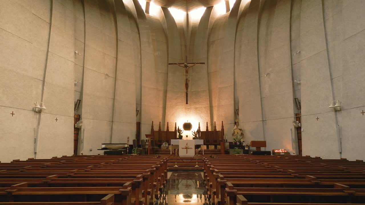 Wide interior gimbal shot of a modern Catholic church in Xàbia, Spain, featuring wooden pews and altar with cross
