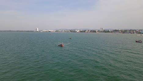 imágenes aéreas inversas de este barco de pesca naranja que también revelan otros barcos en las cercanías y la ciudad de pattaya en tailandia