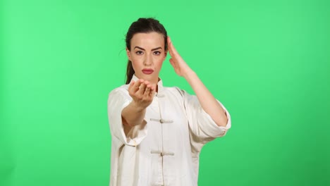 Slow-motion-of-attractive-young-adult-woman-in-white-kung-fu-wushu-uniform-practicing-martial-arts-while-looking-in-camera