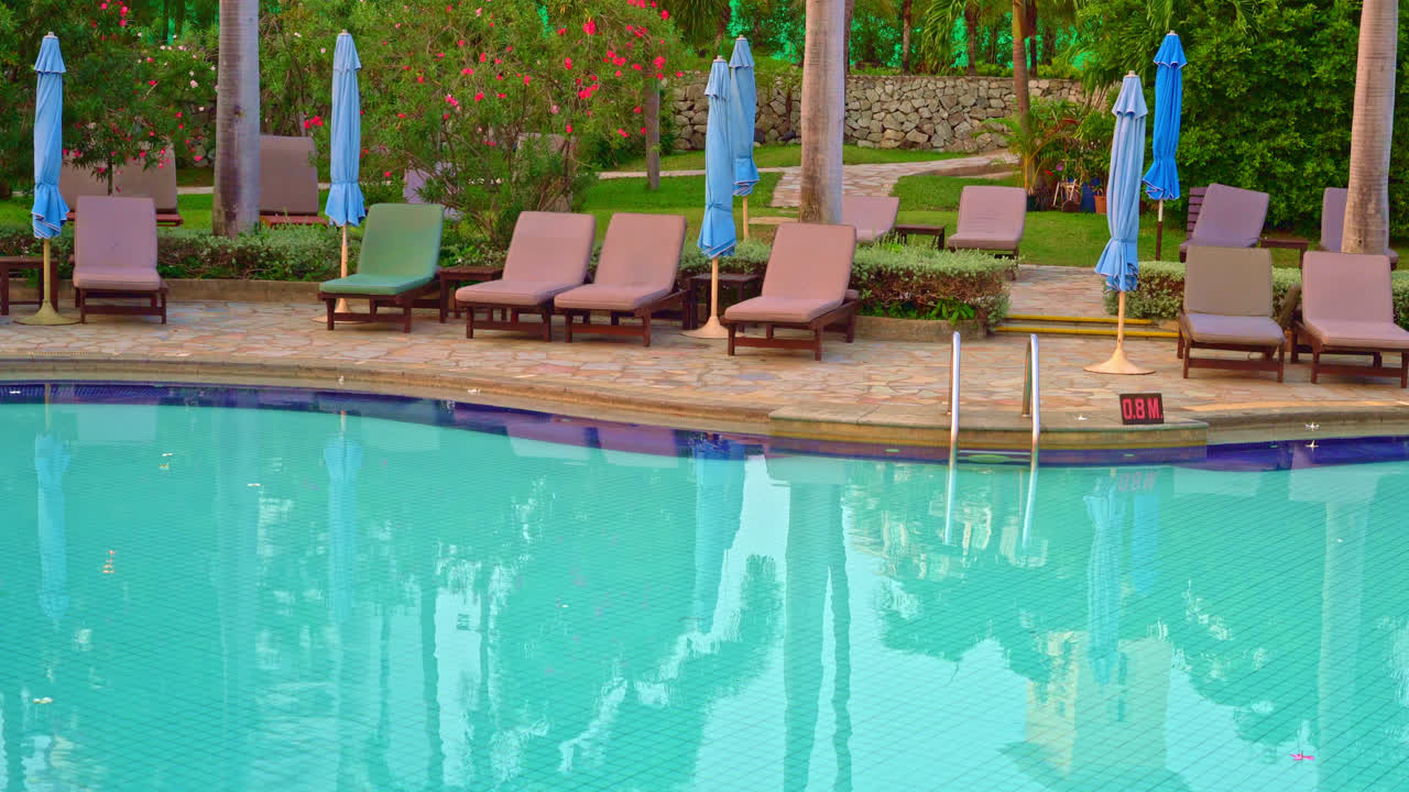 일몰 시간에 수영장 주변에 우산이있는 해변 의자 또는 수영장 침대