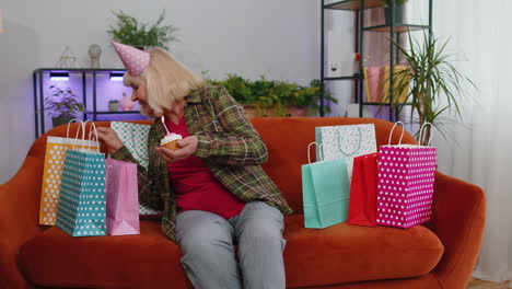 happy senior elderly grandmother woman celebrating birthday party, makes wish blowing burning candle