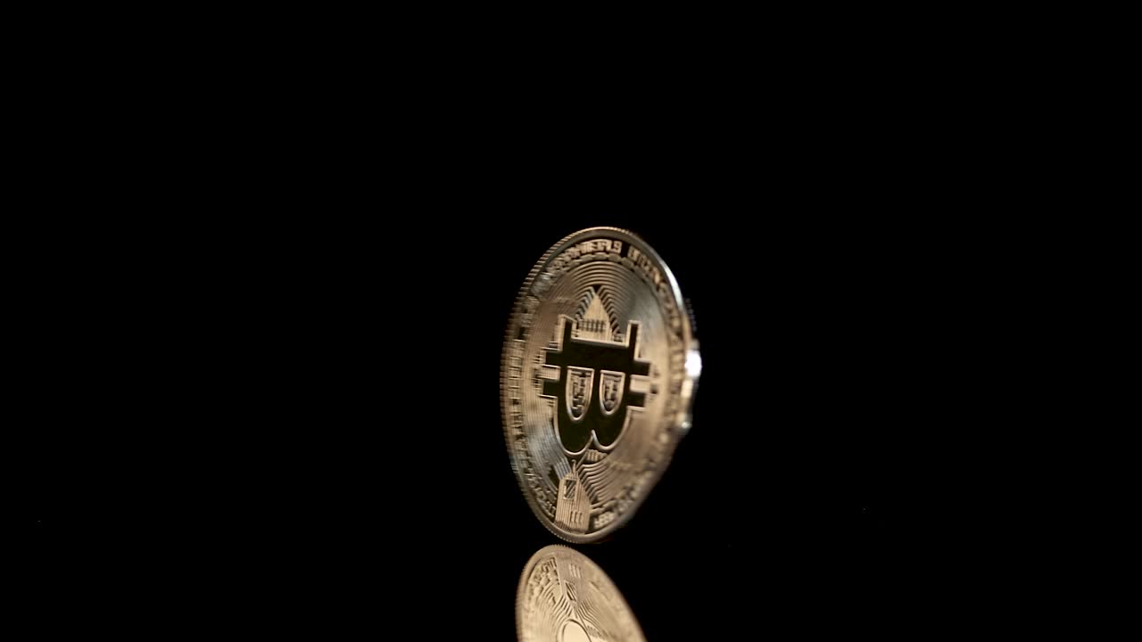 Gold digital coin spins rapidly, illuminated dramatically against a black background with reflective surface