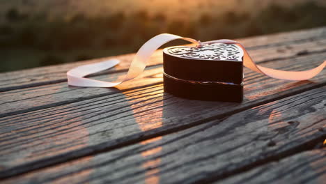 heart-shaped gift box with ribbon on wooden table at sunset