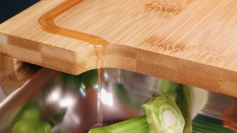 close up of a juice groove with flowing juice from a cutting board with a bowl of cut vegetables and herbs in a modern kitchen