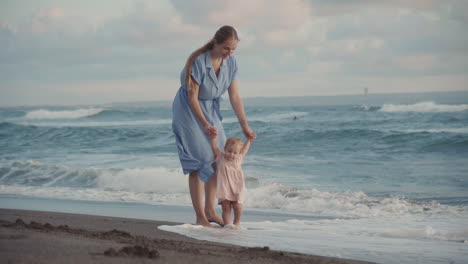 mother helping toddler walk on seashore