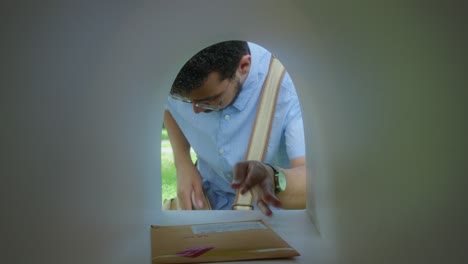 male postal worker putting envelopes into mailbox