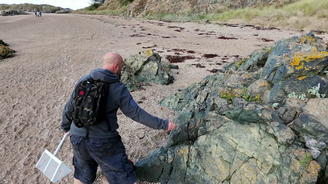 Following man walking dog on beautiful sandy rocky Welsh beach for early morning exercise