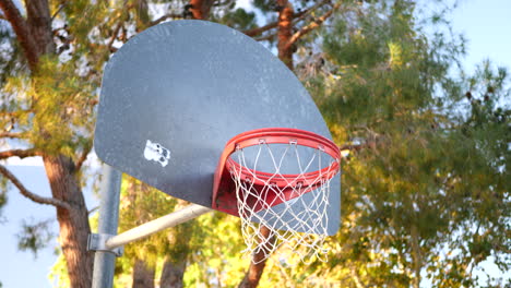 an old basketball hoop with a metal backboard, orange rim and net in an empty park court at sunrise