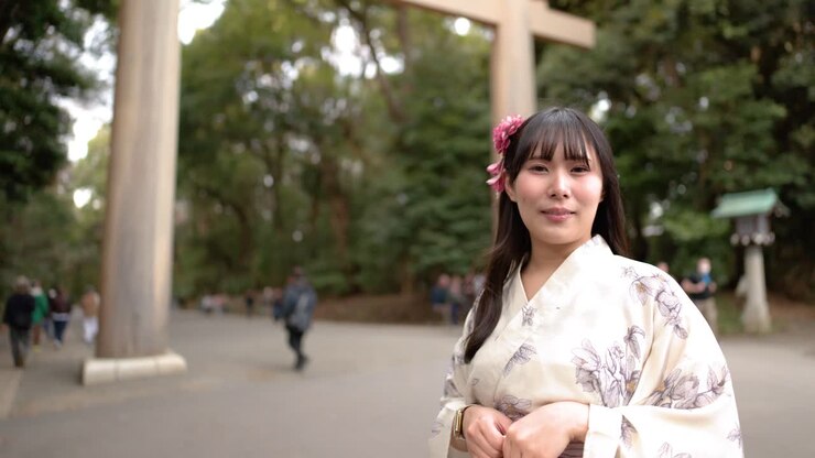 Una donna che indossa uno yukata sta in piedi davanti a un grande cancello torii di legno a Tokyo.