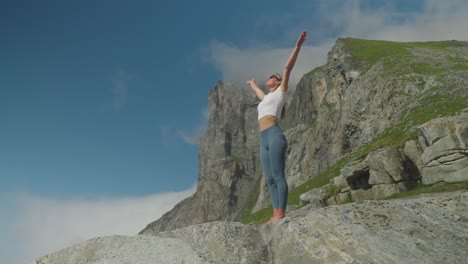 Woman-performs-yoga-sun-salutation-pose-on-rocky-cliff-at-Kvalvika-Beach,-Lofoten,-Norway,-slow-motion