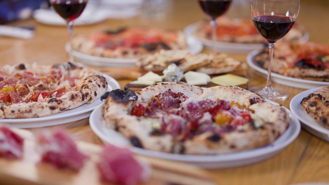 Lenta panoramica della telecamera su pizze a lievitazione naturale, prosciutto e vino rosso durante una cena al ristorante