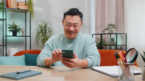 asian chinese mature man sitting on sofa use smartphone share messages on social media application