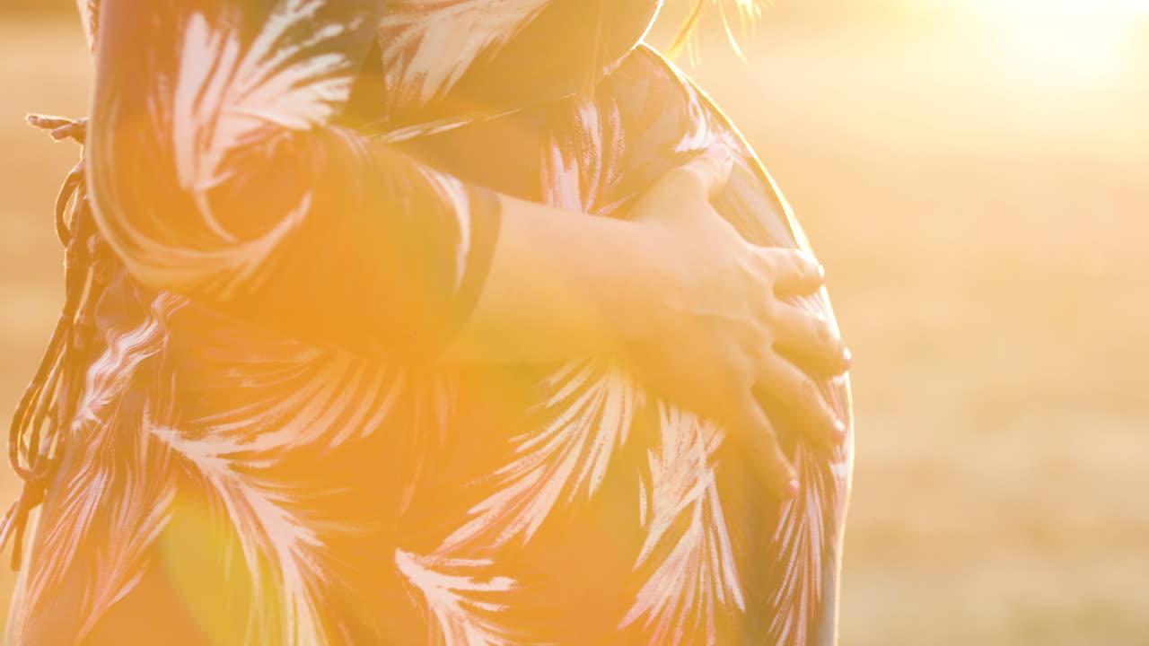 беременная женщина потирает живот во время мирного вечернего заката, когда солнце пробивается сквозь лучи