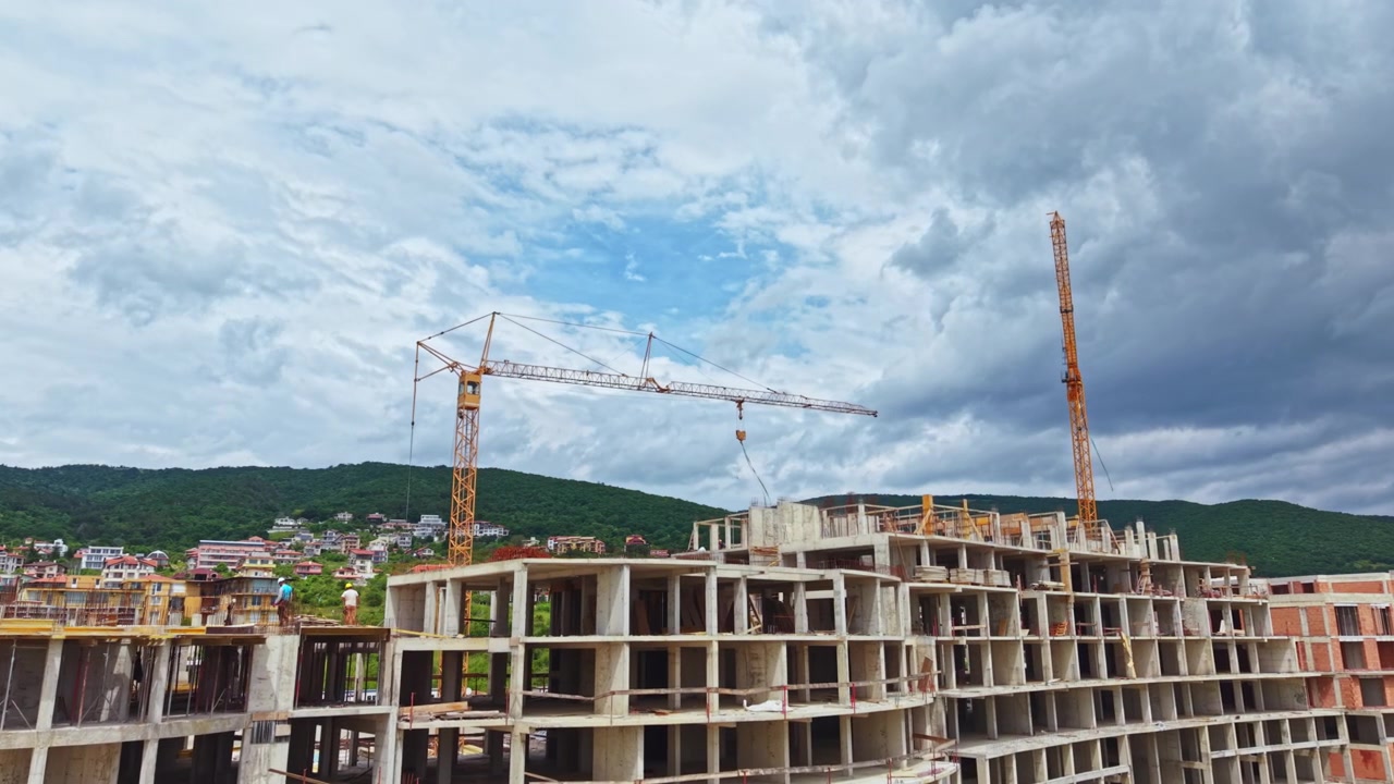 Scena di cantiere. Struttura in cemento incompleta con macchinari e impalcature. Progetto di costruzione industriale con colline distanti e tetti sparsi visibili