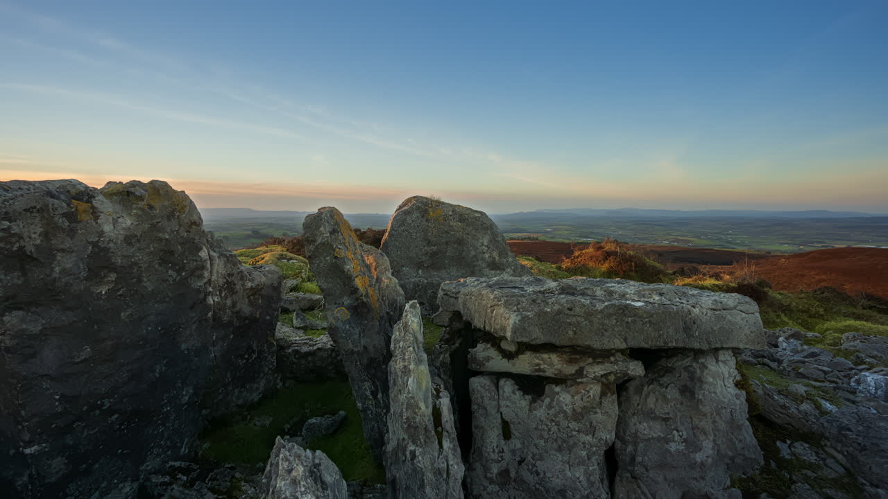 timelapse de movimiento panorámico del paisaje de la naturaleza rural con ruinas de la ruina prehistórica de la piedra de la tumba del pasaje en primer plano durante la puesta de sol vista desde carrowkeel en el condado de sligo en irlanda