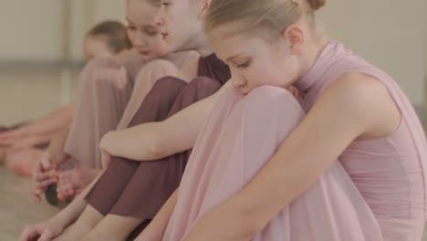 un grupo de jóvenes estudiantes de ballet con ropa de baile negra practicando posiciones en un amplio estudio de ballet con pisos de madera y barras montadas en la pared. expresiones enfocadas y movimientos sincronizados.