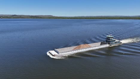 located along the mississippi river between minnesota and wisconsin's driftless area, a towboat moves a barge filled with sand north.