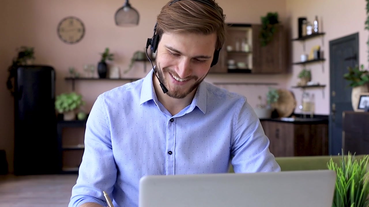 Ung mand med headset arbejder på bærbar computer og tager noter