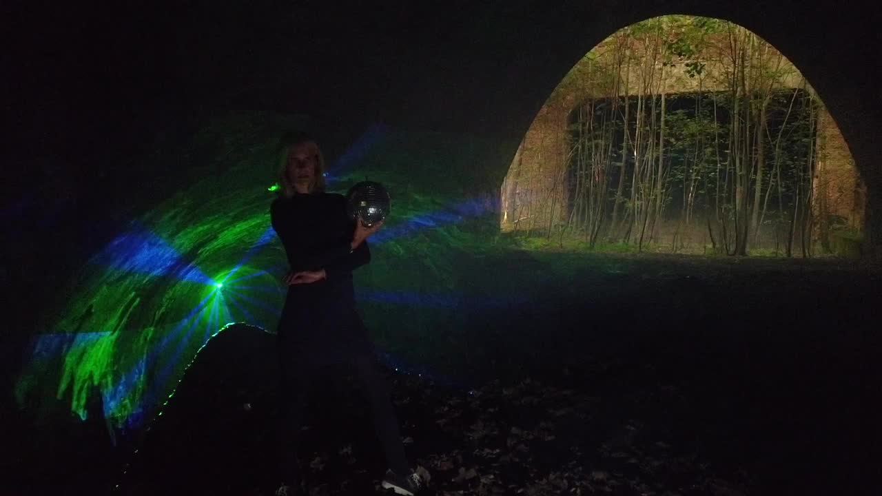 Great slow motion cinematic of a girl with a mirror ball alone in front of a laser at party festival in a russian shooting range. Foto video shoot on lost places in nature 1080, 24p by Philipp Marnitz